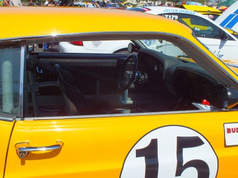 Interior of yellow race car #15 through window showing roll cage and steering wheel
