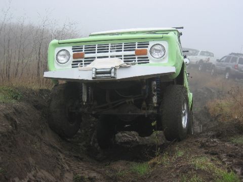 1989 Ford Bronco - A green Ford Bronco navigates a muddy incline with other vehicles visible in the distance.