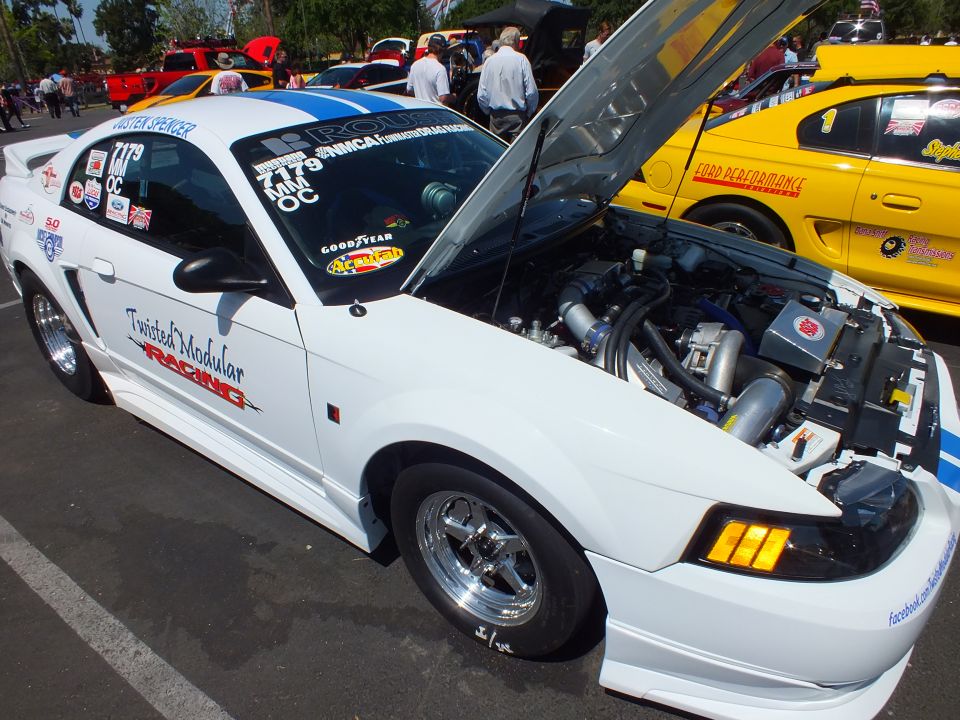 White Mustang drag car with open hood showing supercharged engine, front quarter