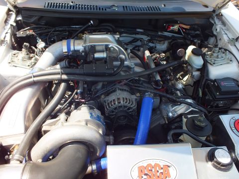 Close-up of supercharged Mustang engine with blue hoses and PSCA-marked bracket