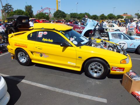 Yellow Mustang race coupe with sponsor decals at car show