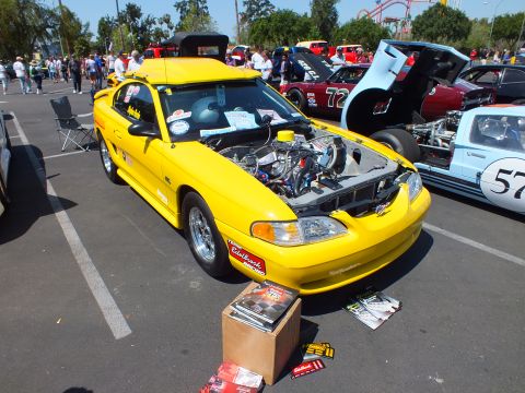 Yellow Mustang with open hood showing supercharged engine at car show