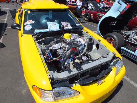 Engine bay of a yellow car with chrome intake and plumbing