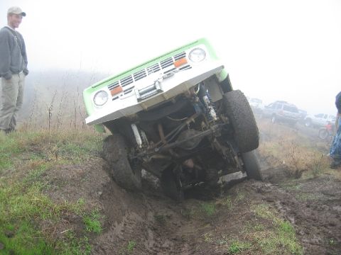 1989 Ford Bronco - A 1989 Ford Bronco is seen tilted on a muddy hill, with other vehicles visible in the background.