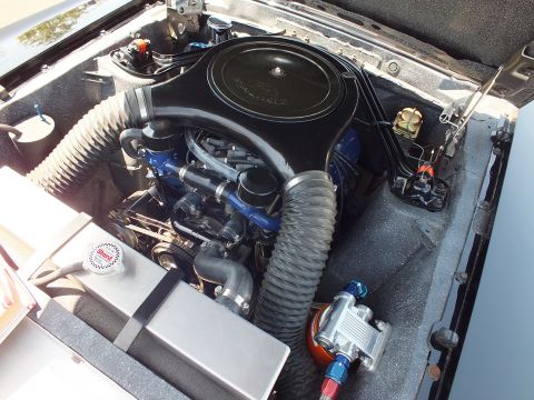 Detailed engine bay of a vintage car with black air cleaner, blue valve covers, and blue braided fuel lines