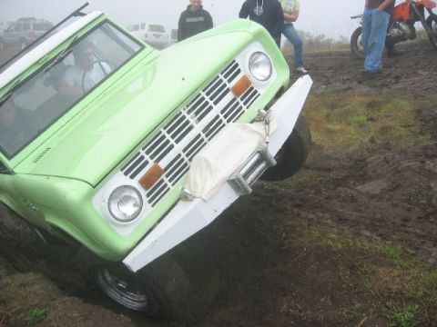 1989 Ford Bronco - Ford Bronco with winch is stuck in the mud, with people and other vehicles around.