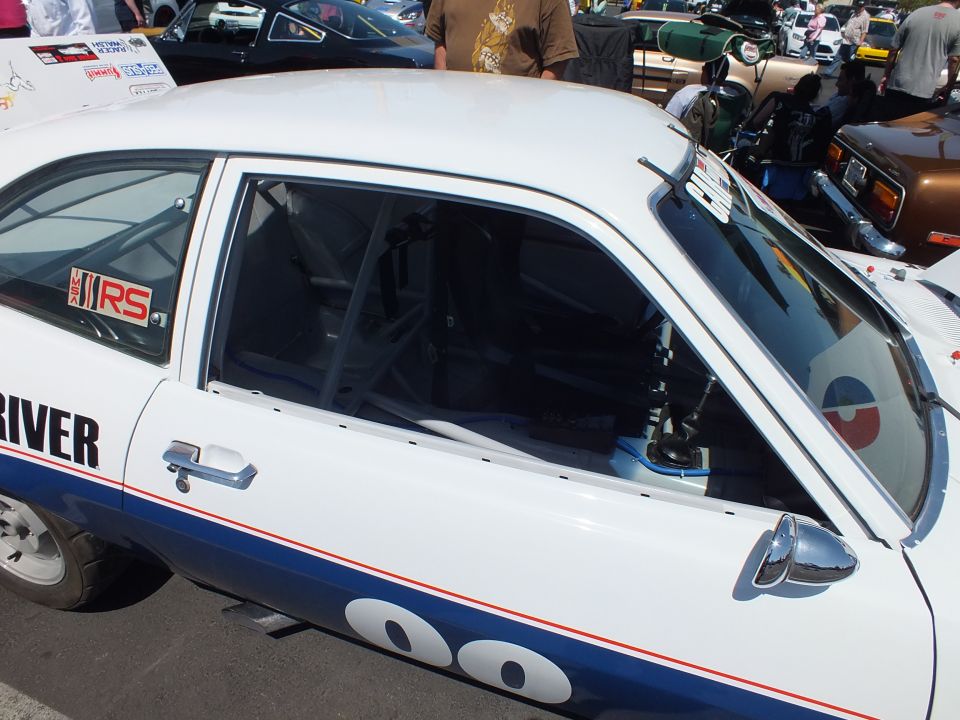 Close-up of a white race hatchback showing roll cage, RS badge and Driver door lettering