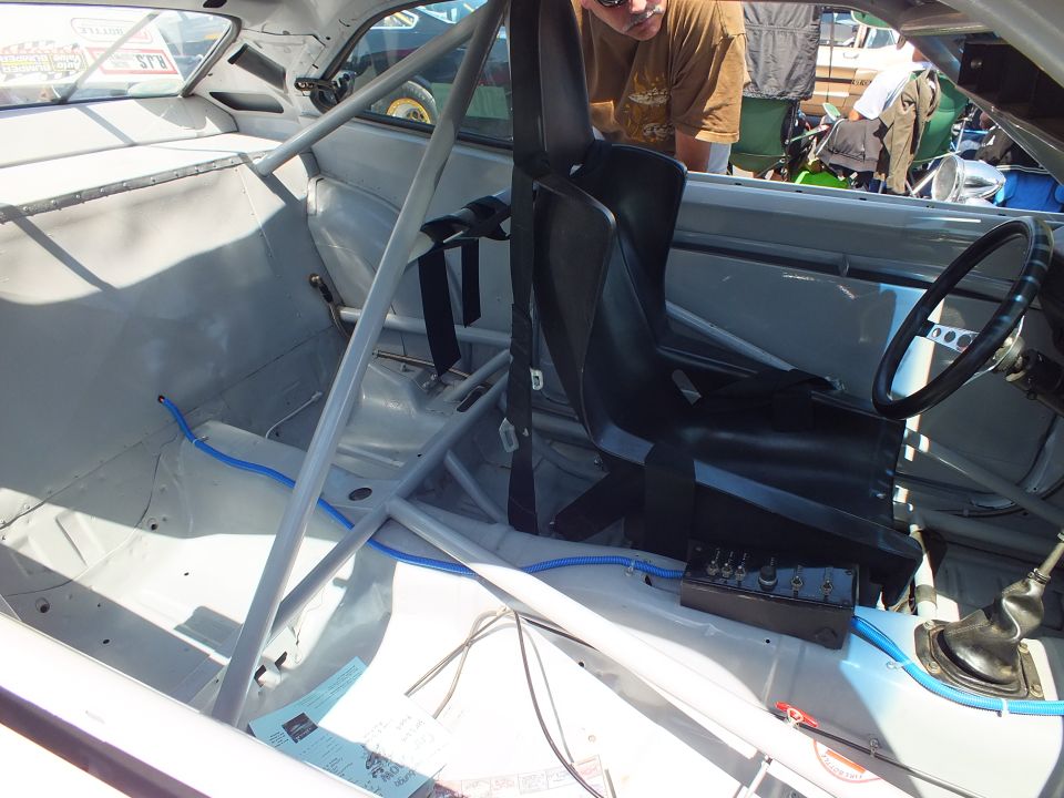 Stripped race car interior with roll cage, single black bucket seat, harness and gear shifter