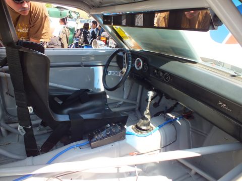 Race car cockpit with roll cage, steering wheel, gauges and tall shifter viewed through window