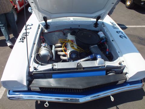 Engine bay of a white race car with 2.3 liter lettering on fenders and chrome bumper