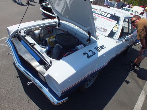 Rear three-quarter of a white race hatchback with open hood and 2.3 liter lettering