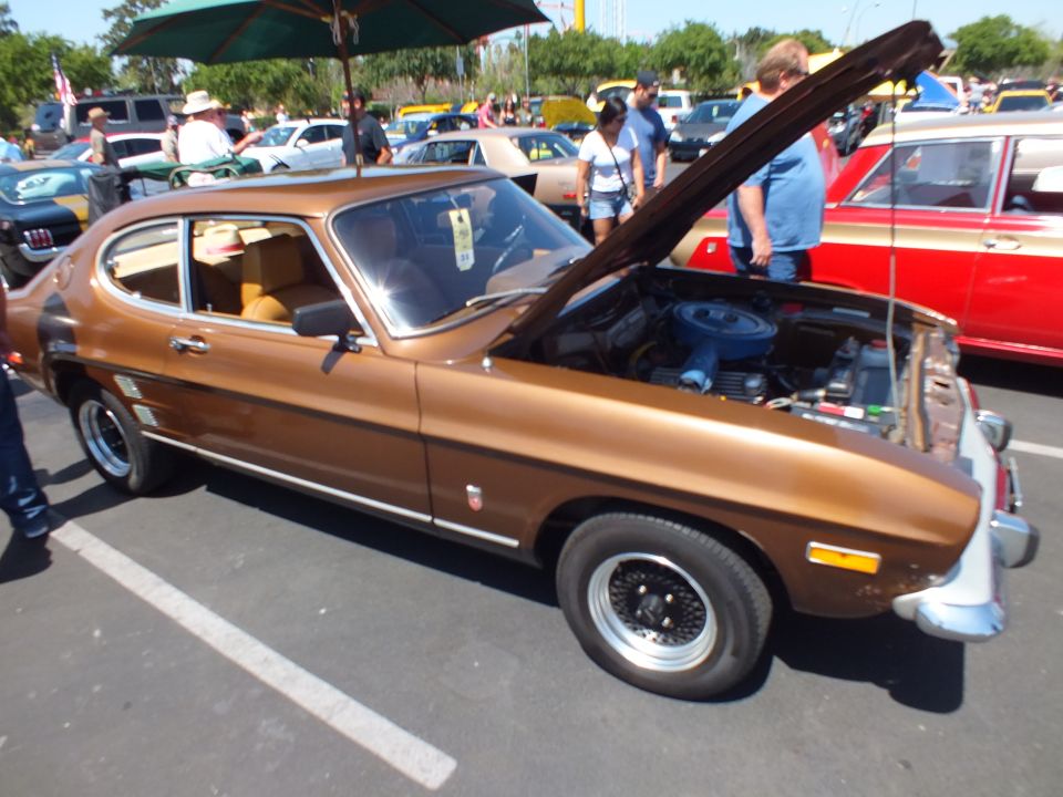 Brown fastback coupe with open hood and tan interior at a crowded car show