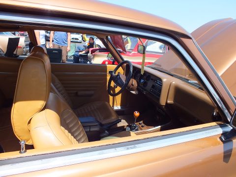Tan leather interior of a coupe showing bucket seats, steering wheel and wood-knob shifter