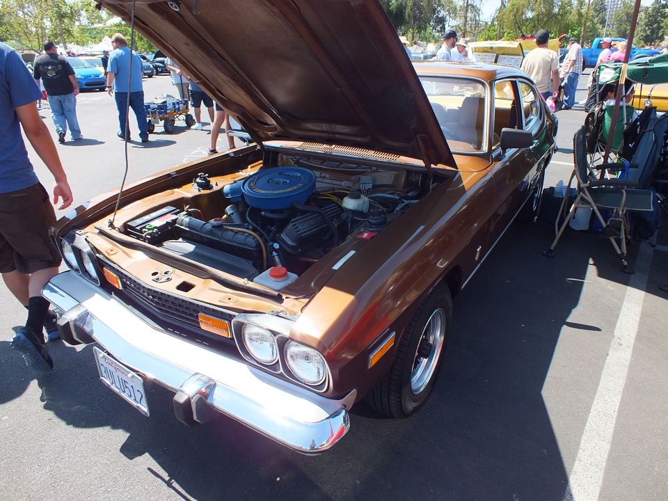 Front three-quarter of a brown fastback coupe with open hood and California plate at a car show