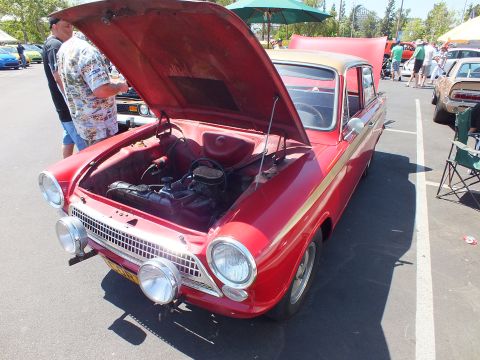 Red two-tone sedan with open hood, round headlights and chrome grille at a car show
