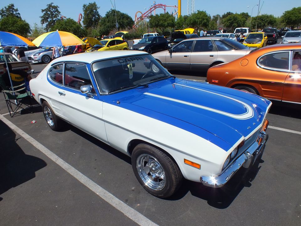 White and blue fastback coupe with bold blue stripe and chrome wheels at a car show