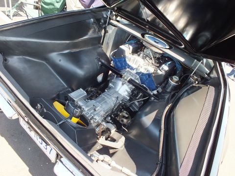Open rear engine bay of black car showing transaxle and V8 with chrome air cleaner