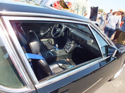 Black sports car interior through side window with manual shifter and blue seatbelts