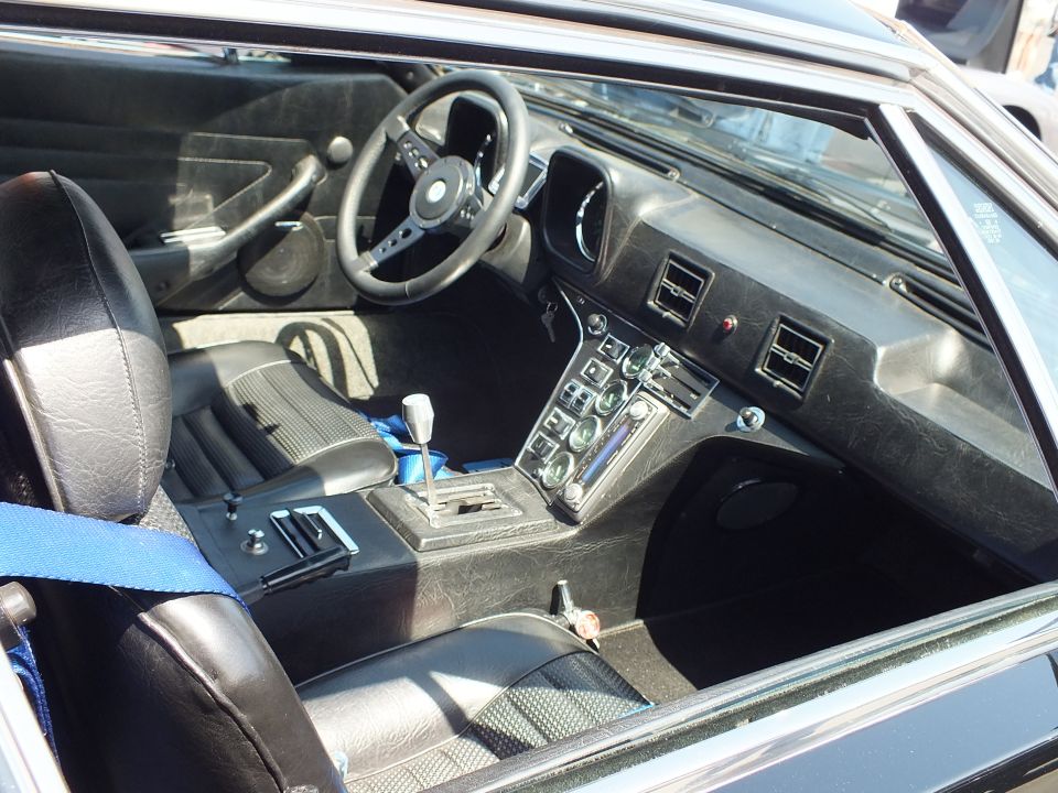 Black sports car cockpit with three-spoke wheel, manual shifter and blue belts