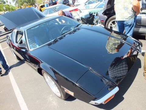 Black wedge-shaped mid-engine coupe from above with engine lid open at car show