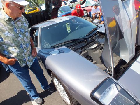 Man in floral shirt views silver Ford GT with open clamshell door at car show