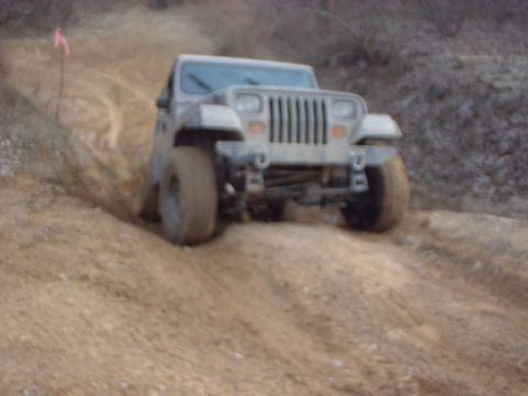 1993 Ford Bronco - A gray Jeep Wrangler navigates a dirt trail, kicking up dust.