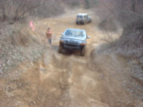 1993 Ford Bronco - A light blue Ford truck with fender flares churns up a steep, deeply rutted dirt hill on a trail, kicking up dust, as two spectators watch…