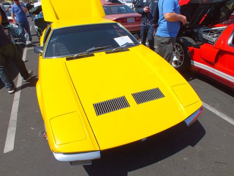 Front of a yellow wedge sports car with raised hatch among show cars