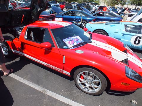 Red Ford GT with white stripes and a magazine on the windshield at a car show