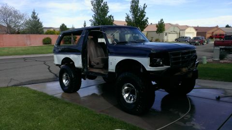 1994 Ford Bronco - This lifted 1994 Ford Bronco features a two-tone blue and white paint scheme and its driver's door is open.