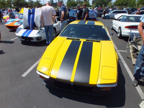 Yellow wedge sports coupe with black racing stripes seen head-on
