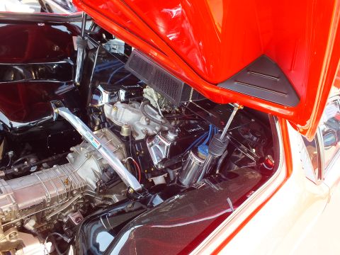 Mid-mounted V8 engine bay of a red sports car with chrome valve covers and red intake