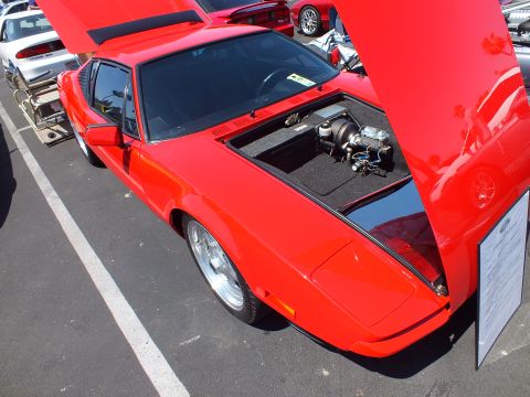 Red mid-engine sports car with rear engine cover open at an outdoor car show
