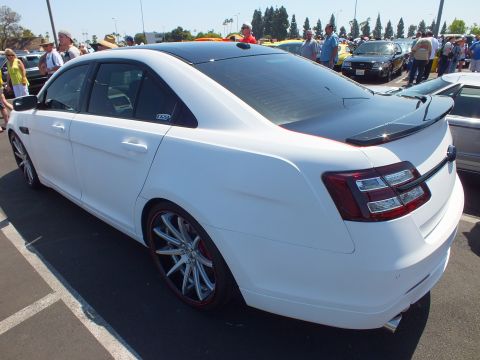 Rear quarter of a white Ford Taurus sedan with lip spoiler and chrome wheels