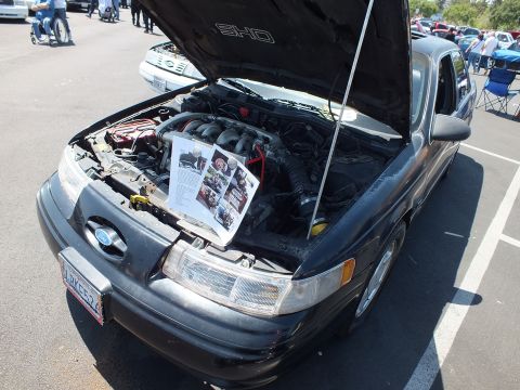 Black Ford Taurus SHO with hood up showing V6 engine at outdoor car show