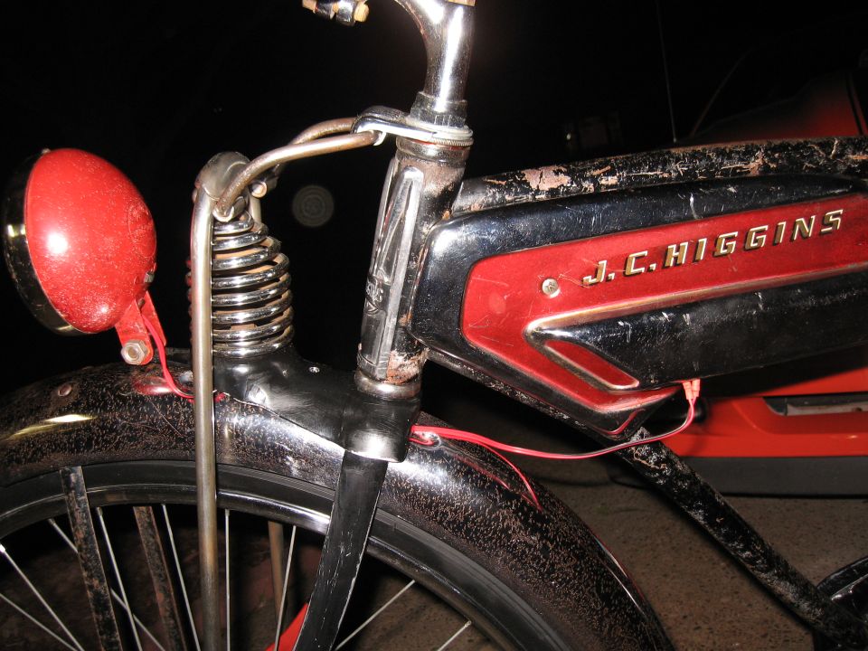 Close-up of J.C. Higgins bicycle frame with red and black paint, chrome handlebars, and a red headlight