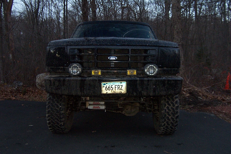 Front view of a black Ford F-Series truck with a custom bumper and off-road tires. License plate reads 665-FRZ