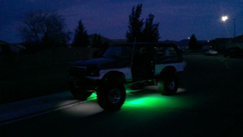 1994 Ford Bronco - A modified Ford Bronco with green underglow lighting is parked on a street at dusk.