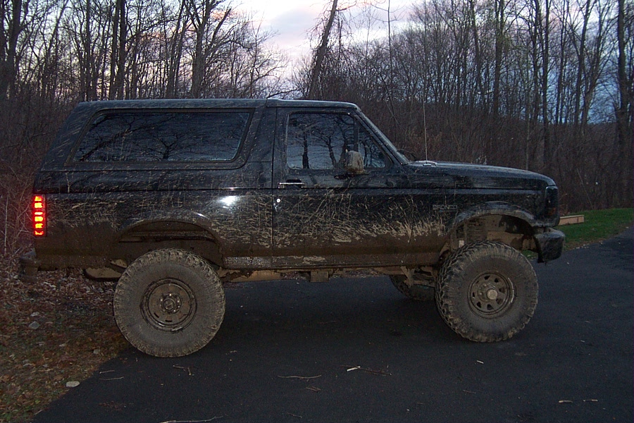 Mud-splattered black Ford Bronco, side view, with aftermarket wheels and tires