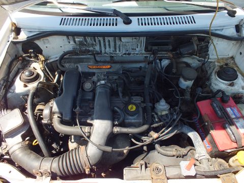 Engine bay of small white car showing inline four-cylinder engine