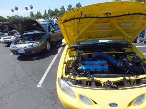 Yellow Ford coupe with hood up showing blue engine at car show