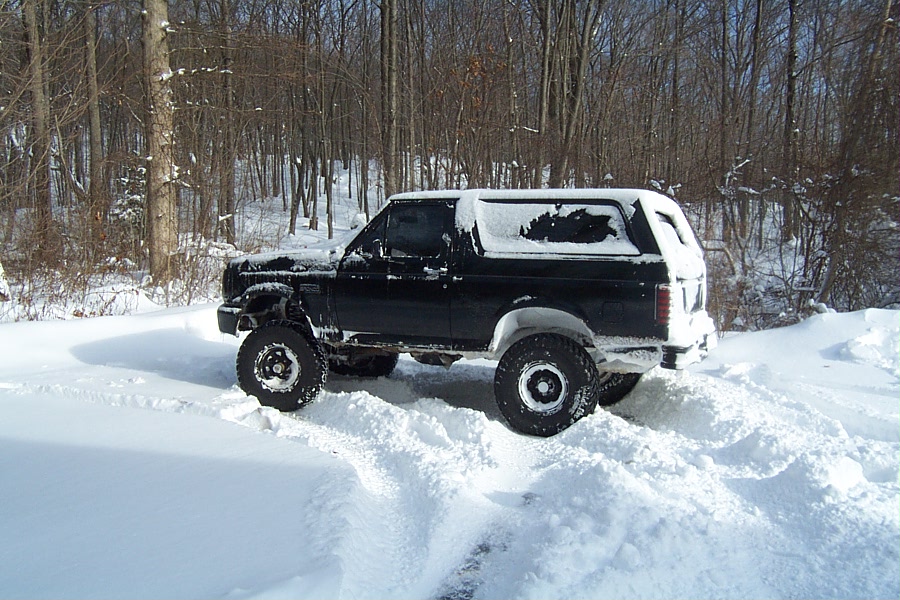 1996 Ford Bronco driving through deep snow, trees in background