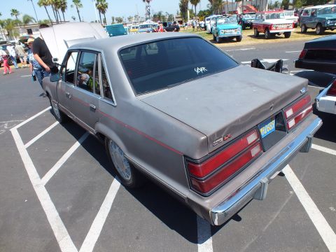 Rear three-quarter of a gray 1980s Ford four-door sedan in a car-show parking lot