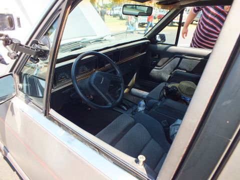 Interior of an older car showing steering wheel, gauges and gray cloth seats