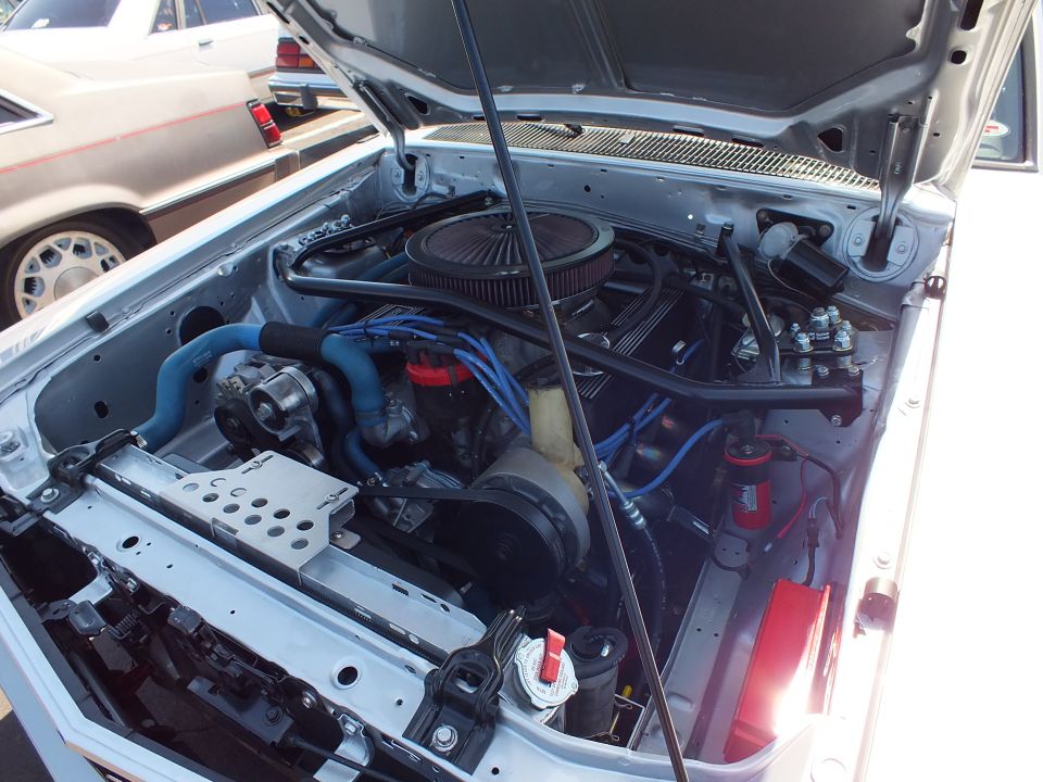 Engine bay of a white car with round air cleaner and blue plug wires