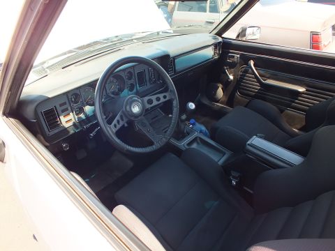 Car interior showing black dash, three-spoke wheel, gauges and bucket seats
