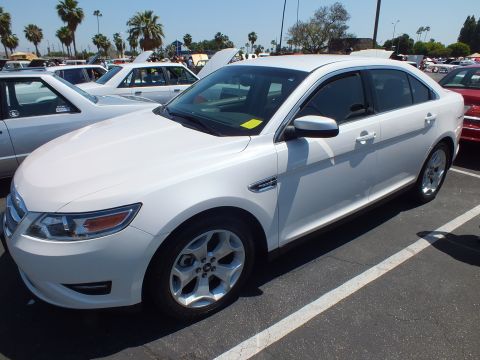 Front three-quarter of a white Ford Taurus sedan among rows of cars