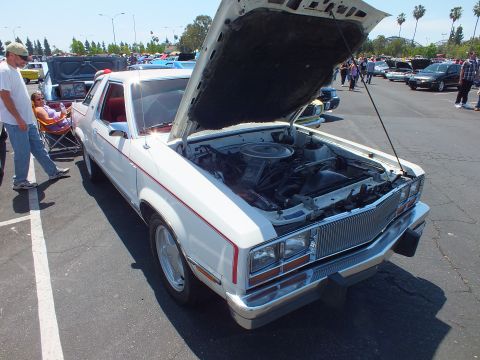 White 1980s Ford coupe with hood up and red interior at a car show