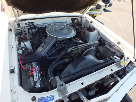 Engine bay of a white car with round air cleaner and red battery cable