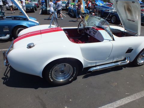 White Cobra-style roadster with red stripe and red interior, hood open, at a car show
